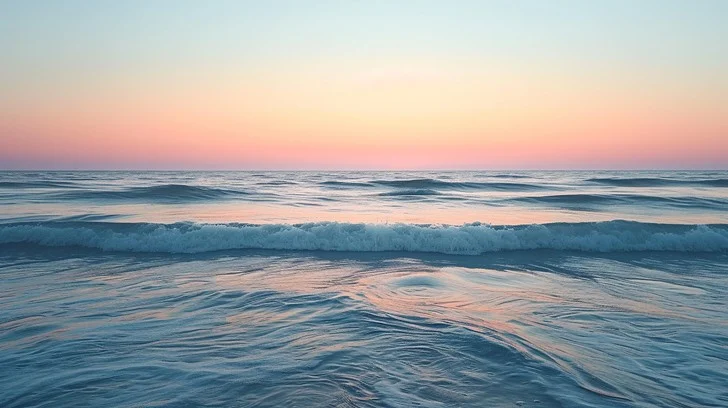 Misty ocean shoreline at dawn with soft waves and calm horizon
